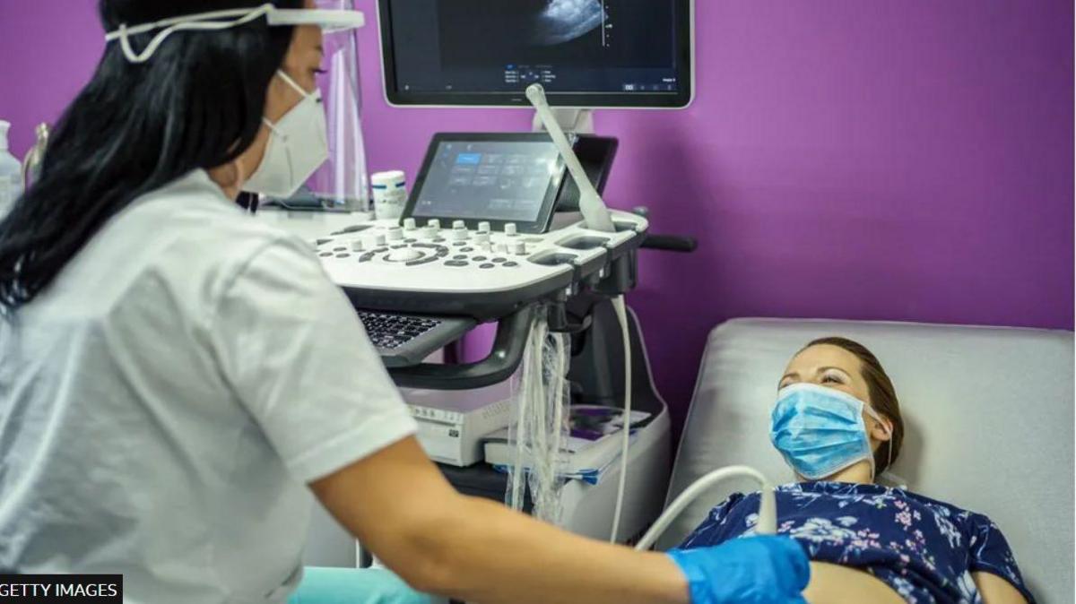 A pregnant woman gets a pre-natal scan alone in hospital, wearing a face mask