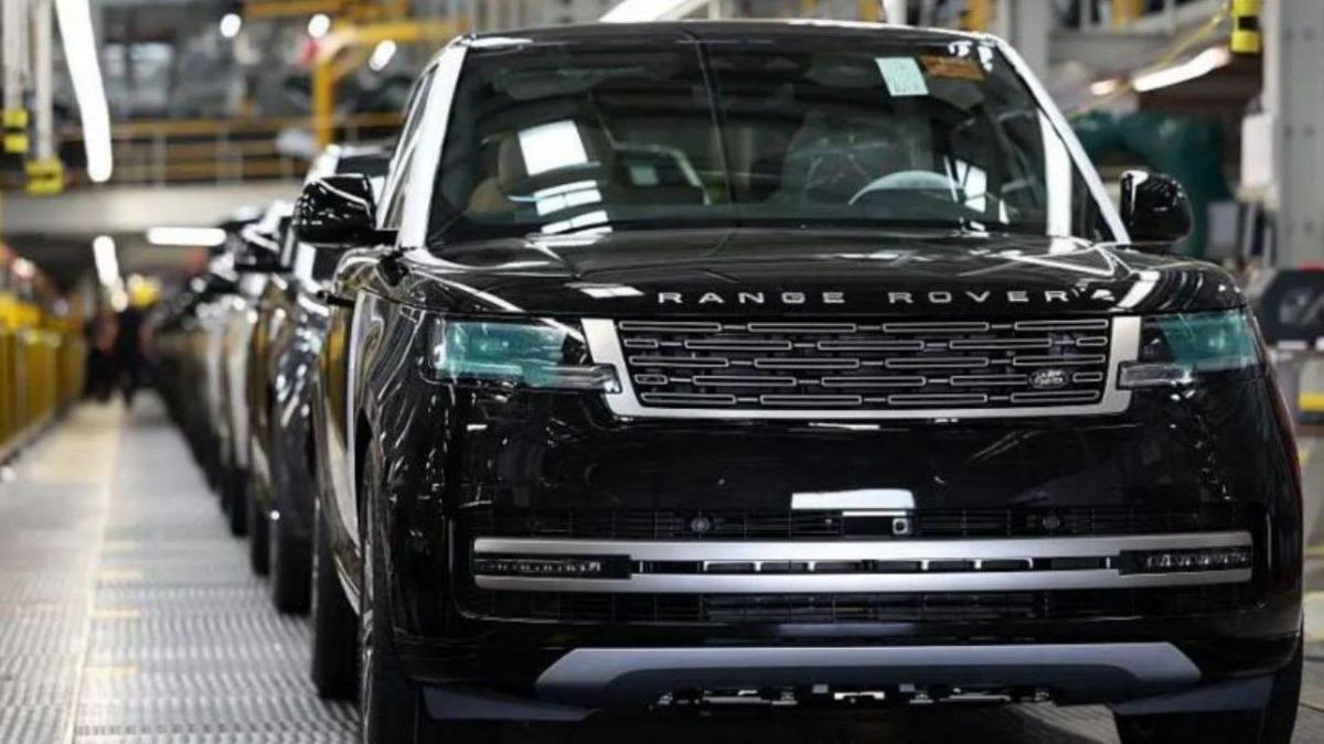 A black Range Rover is at the front of a factory production line that has a metal walkway, on the left, running alongside the vehicles that are in a queue.
