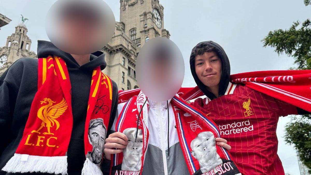 Three young lads pose in a line for a photo at the Liverpool parade with football shirts and scarves, with Mason Osborne on the right. The faces of the other two are blurred out to protect their identity.