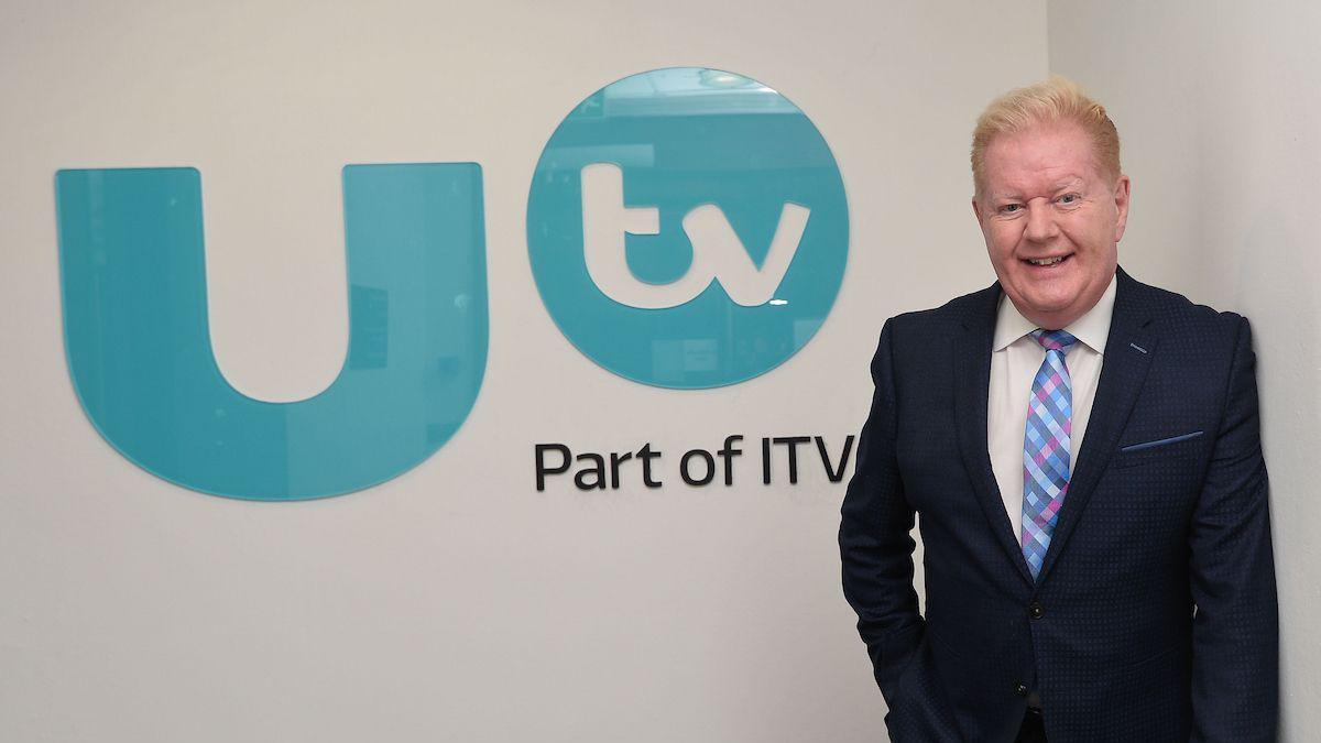 Julian Simmons wearing a suit and tie standing beside a UTV logo