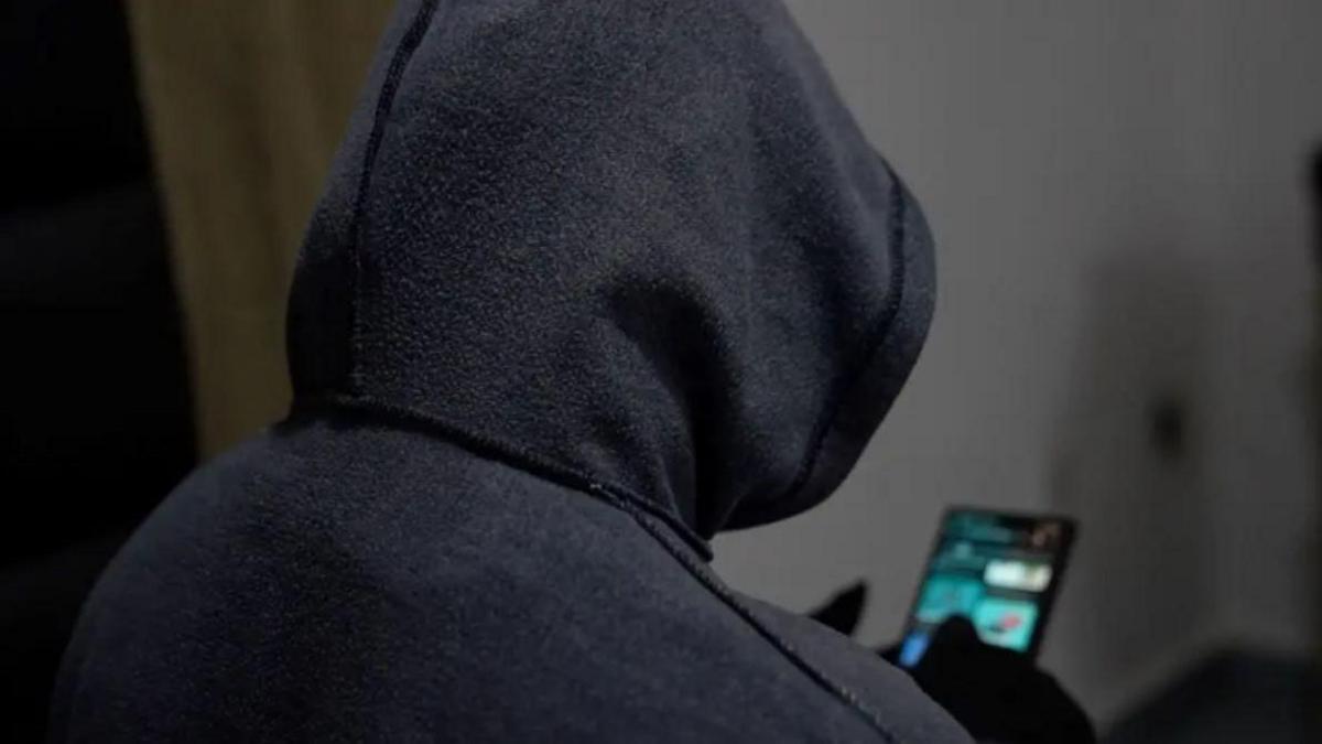 A hooded figure with back to camera on a mobile phone