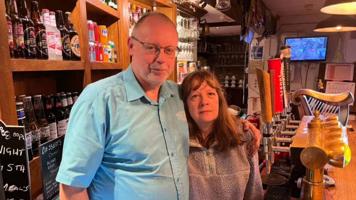 A bald man wearing a blue shirt stood next to a woman with brown hair