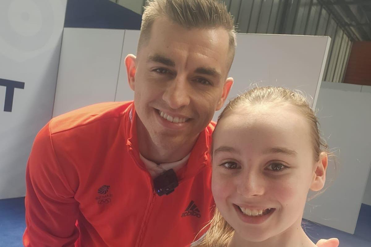 Amelia is posing with Max Whitford. He's wearing bright orange. They're both smiling.