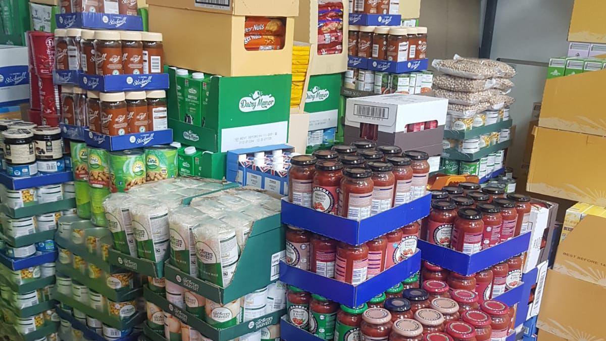 Large amounts of tinned and jarred food, all in boxes, piled in a room. 