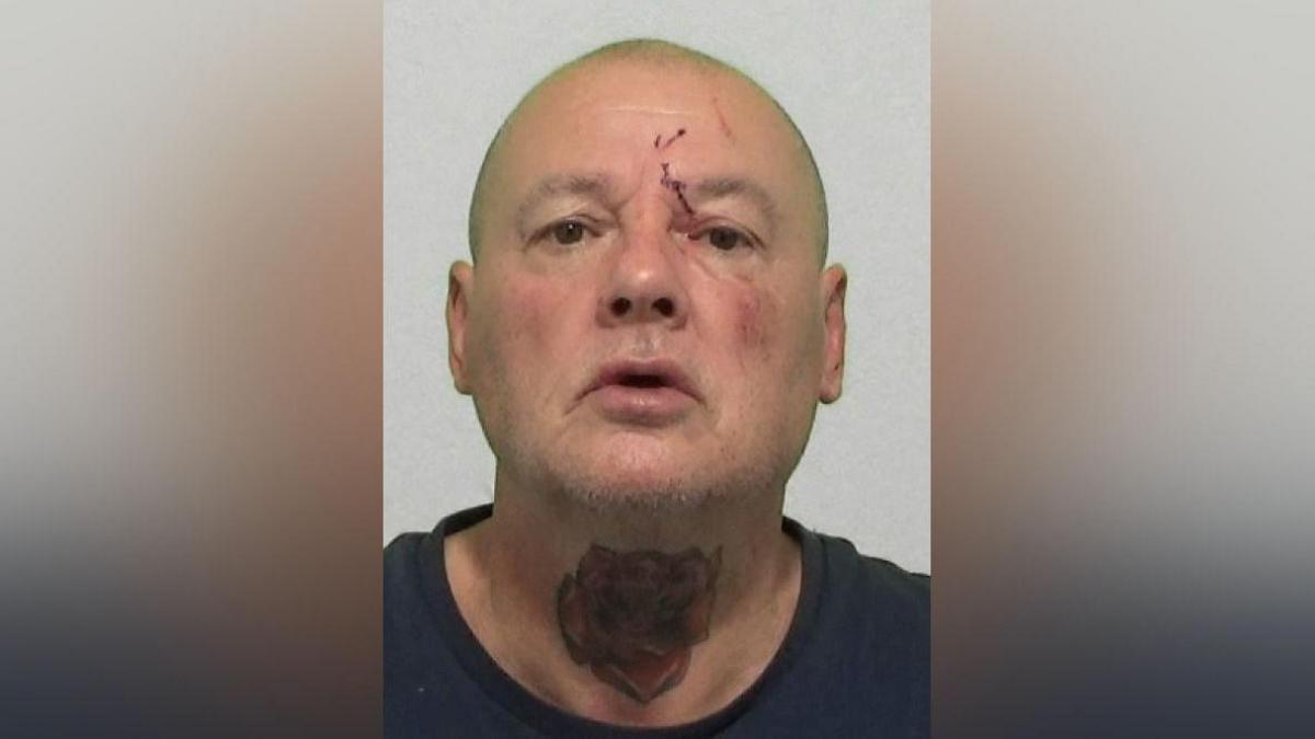 Mugshot of Straughan. He is bald with a cut above his left eye and a large red rose tattooed across the front of his neck