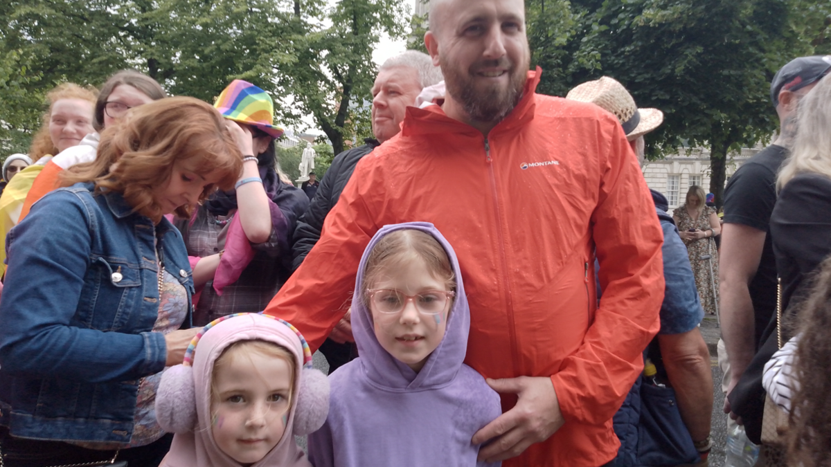 Man with his arms around two young girls amongst a crowd 