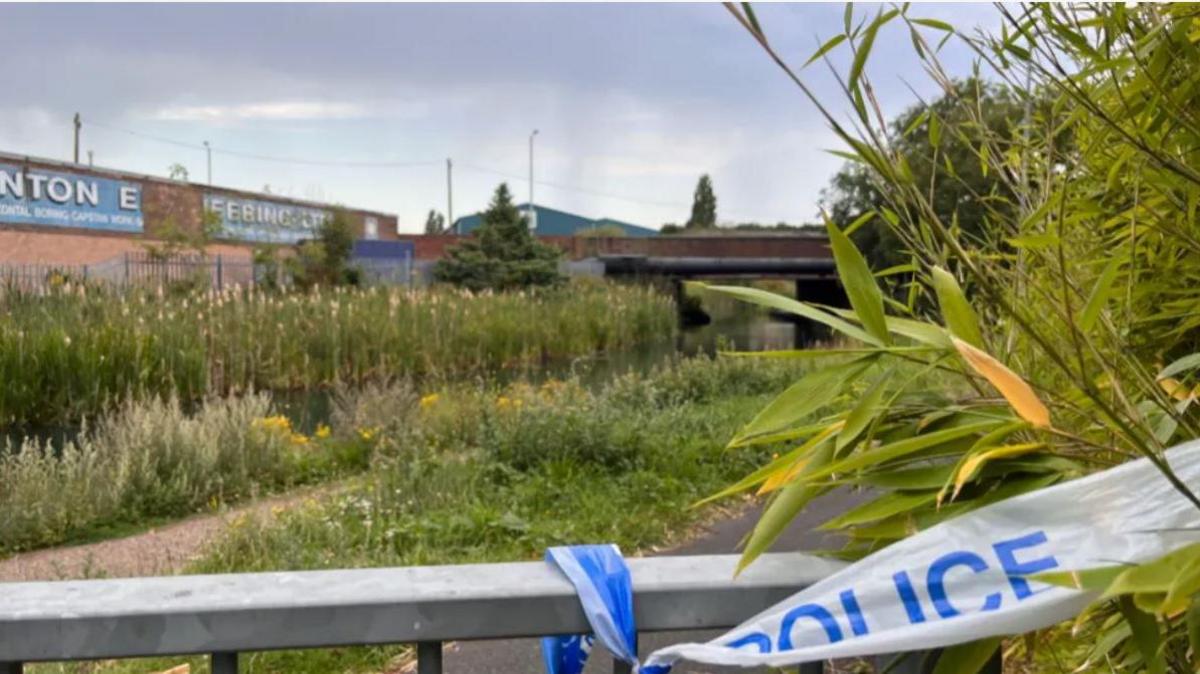 Police tape on a silver railing about five yards from a canal