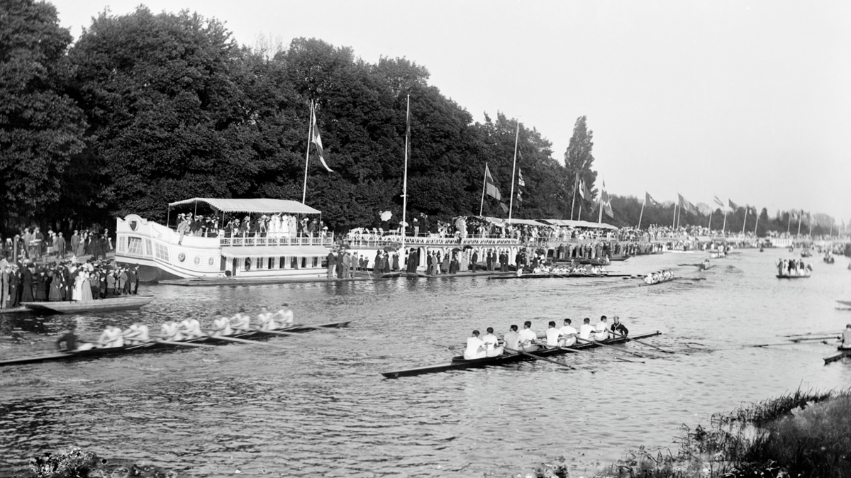 A black and white image of spectators on the college barges and the riverbank watching a boat race during Eights Week in Oxford, around 1860-1922.