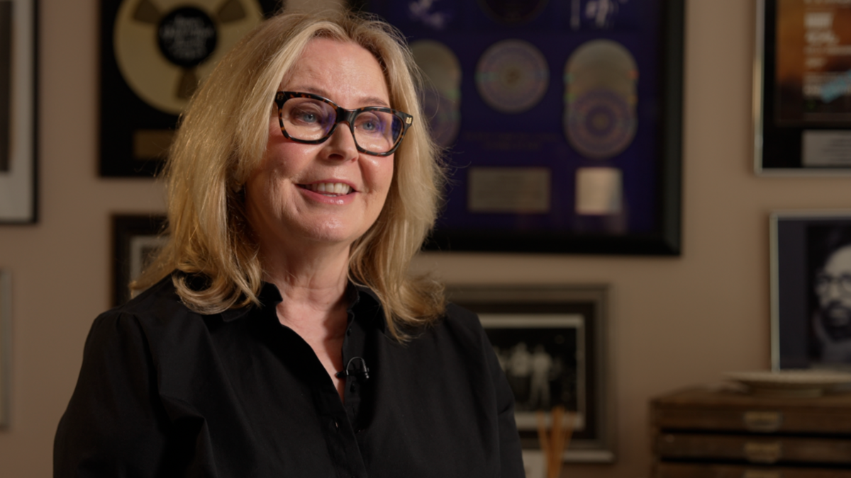Tessa Niles from Maidstone, who was a backing singer on the day of Live Aid 40 years ago. She has blonde hair and is wearing a black shirt. Pictured albums can be seen in the background.