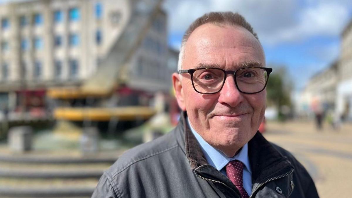 Tudor Evans, Labour leader on Plymouth City Council, in a blue shirt and burgundy spotted tie with a grey jacket and wearing glasses, in Armada Way in Plymouth.