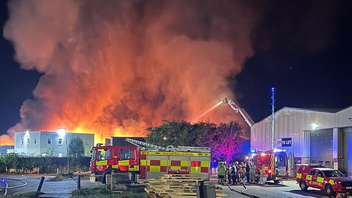 A red fire truck in front of a building on fire with red plumes of smoke