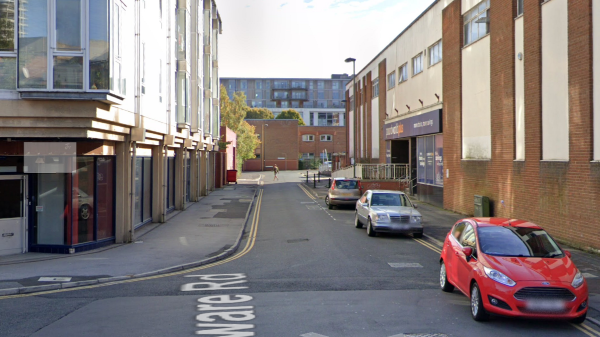 A google maps street view shot of Edgeware Road in Swindon. There are three cars parked along the side of the road and buildings lining the street, as well as straight ahead. 