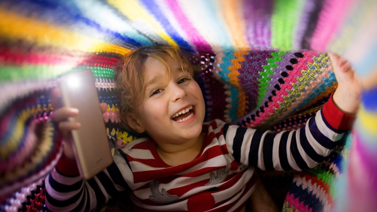 Boy with a smartphone under a blanket