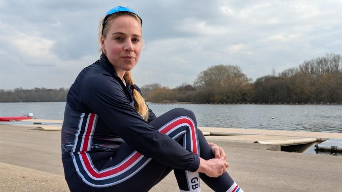 Becky Wilde sits on the edge of a rowing dock with her arms wrapped around her legs