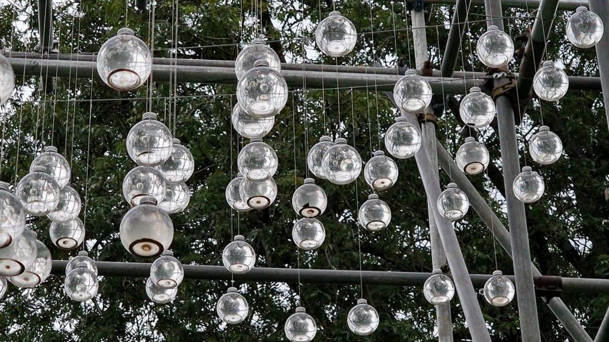 Hundreds of spherical bottles of water and chalk sediment suspended by think cords from a metal frame