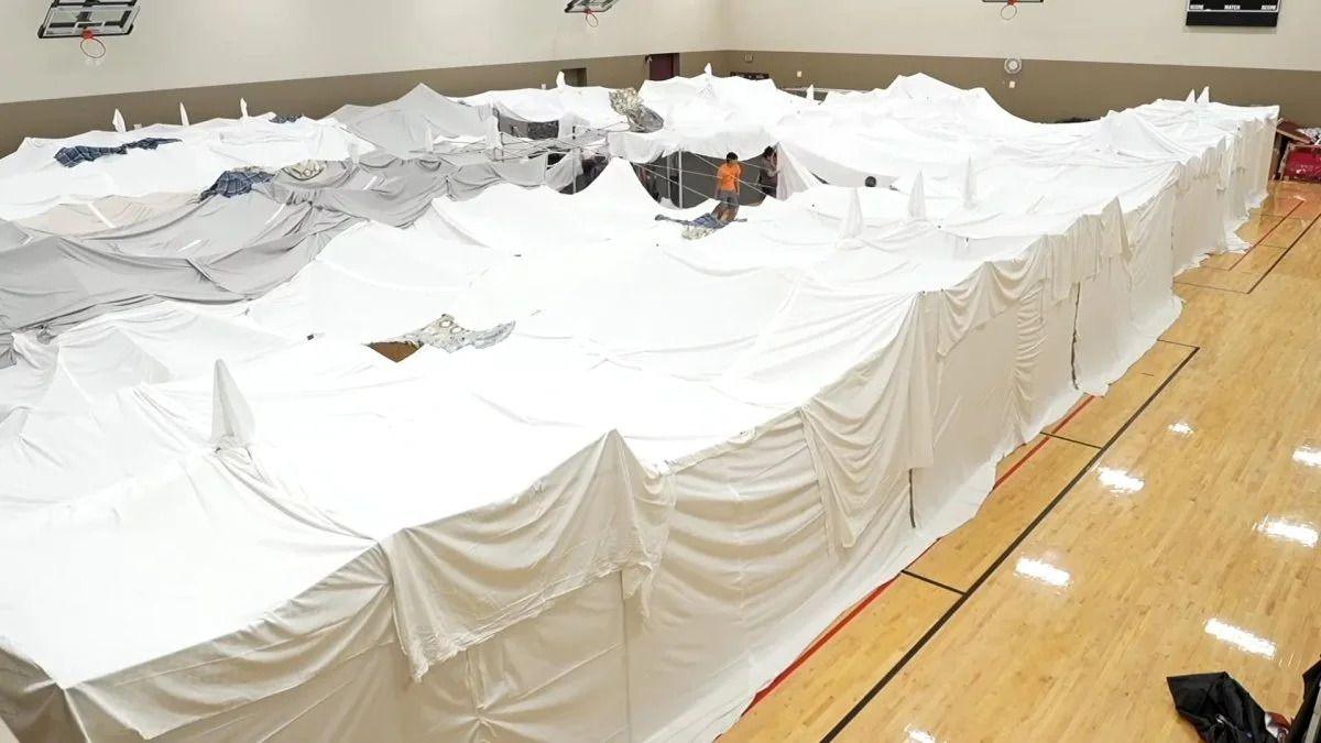 A large blanket fort made of white sheets sits on a polished wood floor.