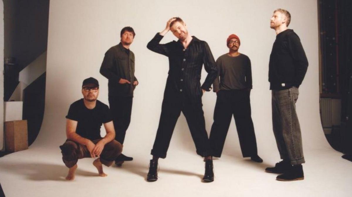 Picture of members of the band Kaiser Chiefs - four out of five are standing up in front of a white background. All are wearing black or grey clothing.
