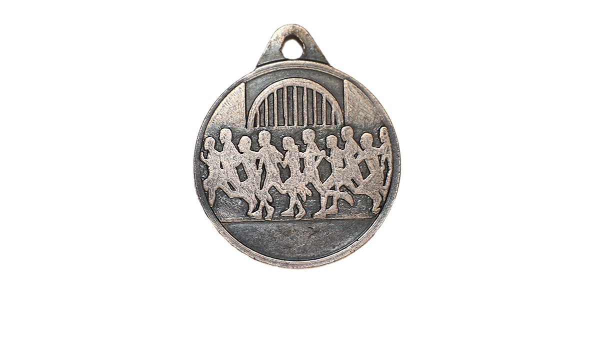 A silver circular medal with carvings of people running and on top is a bridge.