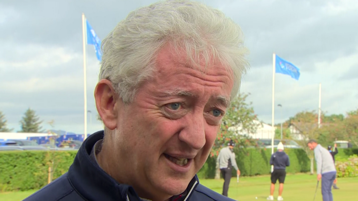 John McGrillen is looking past the camera. He has white hair and is wearing a navy jacket. People are playing golf behind him.