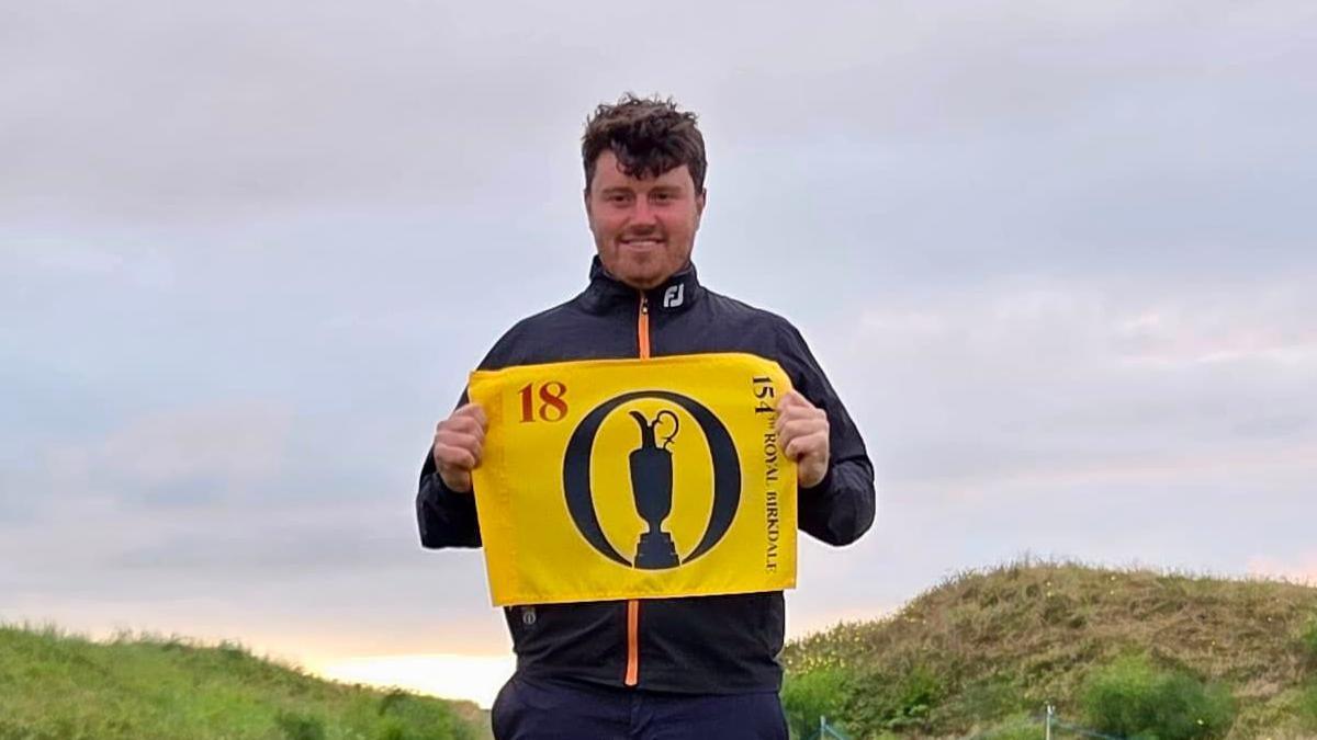 Tom Sloman holding a yellow flag with the figure 18, The Open Championship logo, and 154th Royal Birkdale written on it.