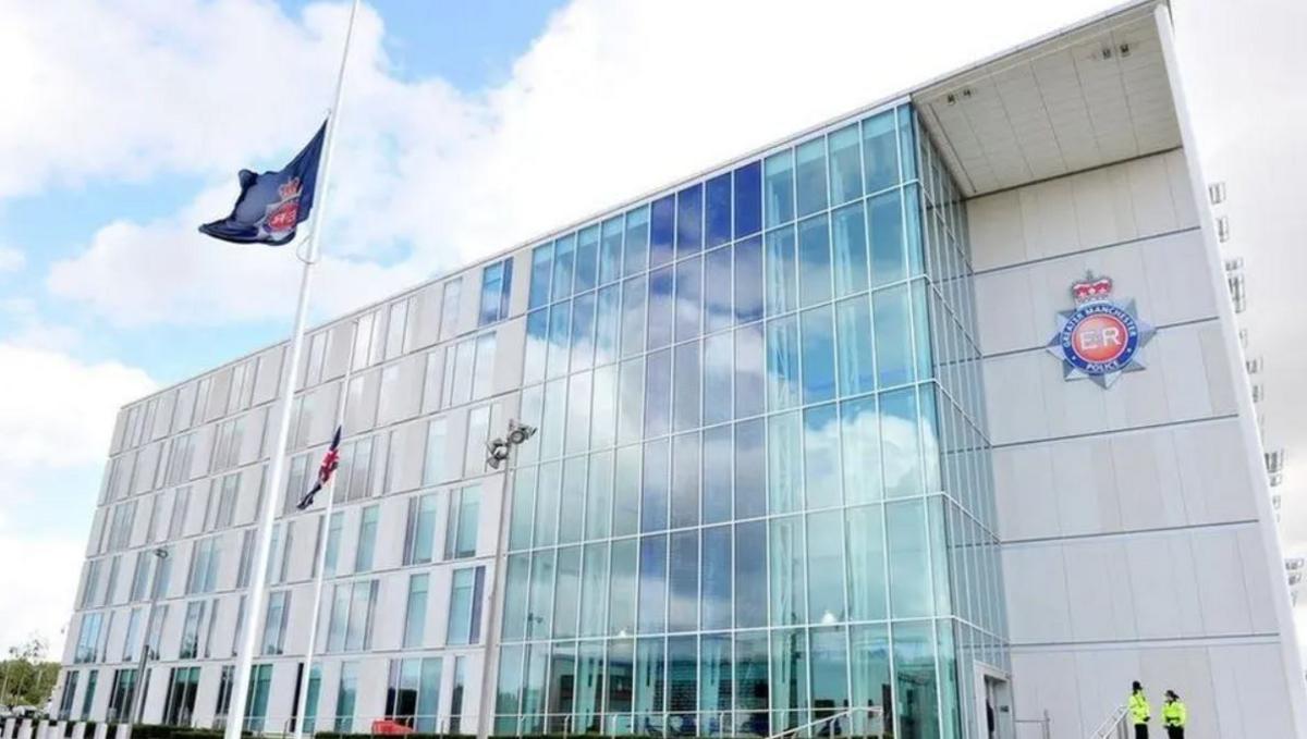 The exterior of Greater Manchester Police's headquarters in Manchester flying a flag with the force's logo and a sign with the log on the building. Two police officers said outside the building