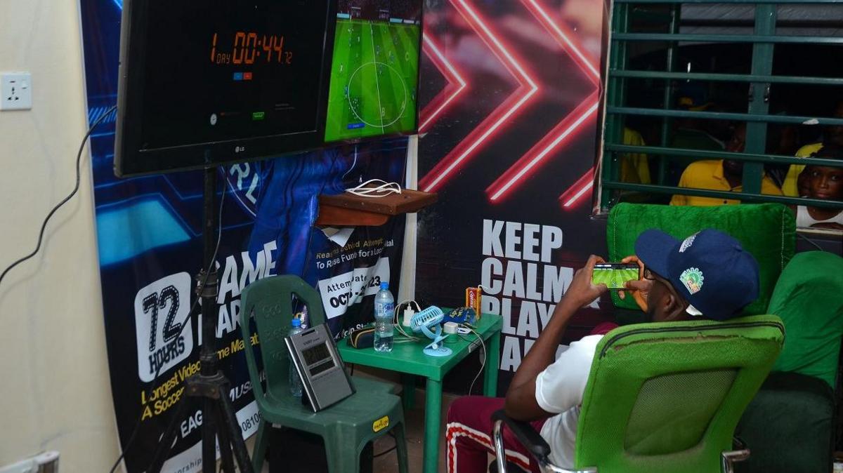 man plays football videogame as people watch through the window.