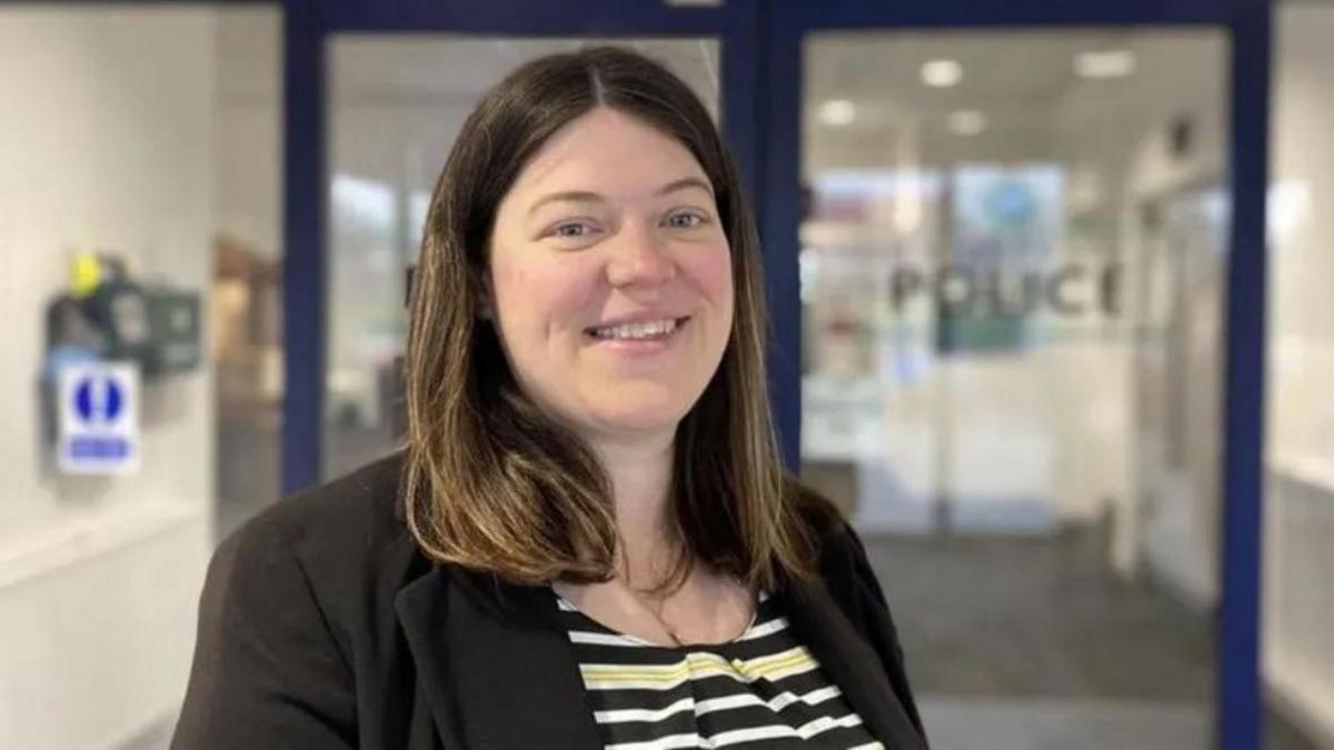 Emily Spurrell. Woman with long brown hair wearing a black and white striped top and black suit jacket.