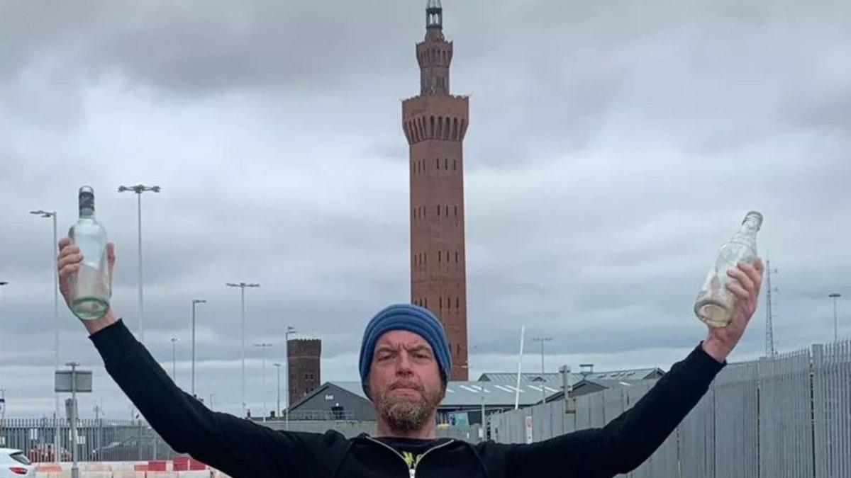 A man holds two glass bottles near the Grimsby Dock Tower