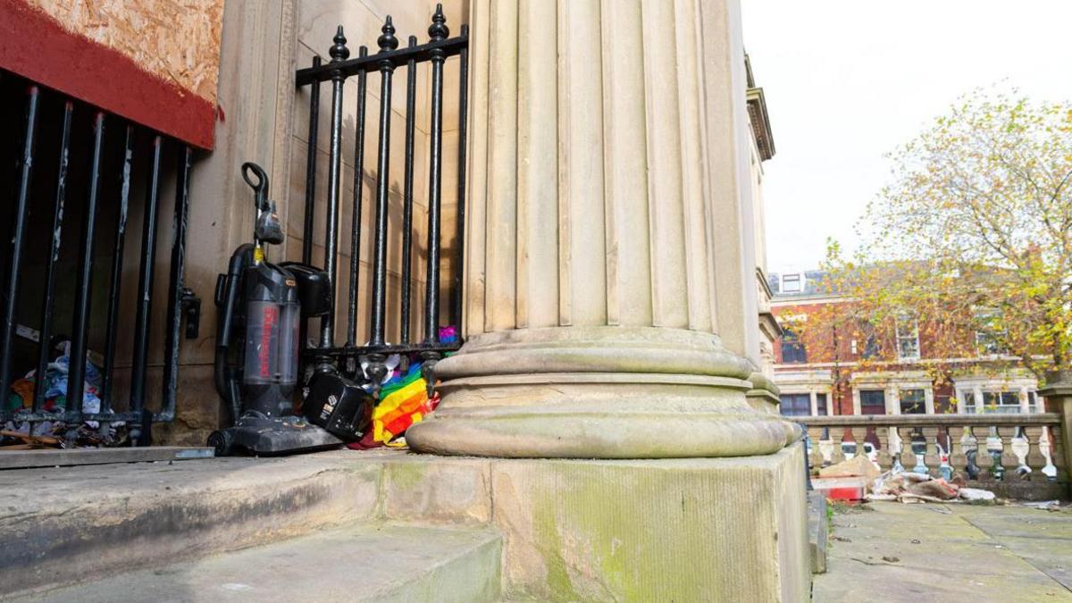 A disgarded hoover and rubbish lay at the entrance of a stone building