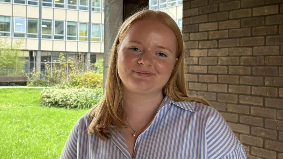 A head-and-shoulders shot of Isobel, outside her office at work, smiling into the camera. She has long, strawberry-blonde hair and wears a striped blue and white shirt.