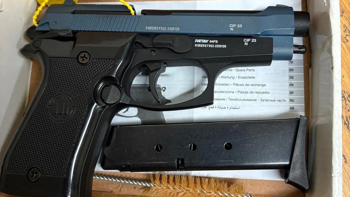 A black and blue automatic pistol, an ammunition magazine and a barrel cleaning brush in a box