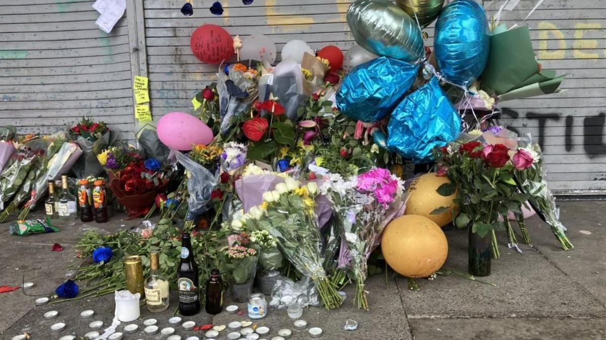 Flowers have been left near the scene of the crash. There are a number of tealights on the floor and bottles of drinks. Colourful balloons have also been attached to some of the flowers.