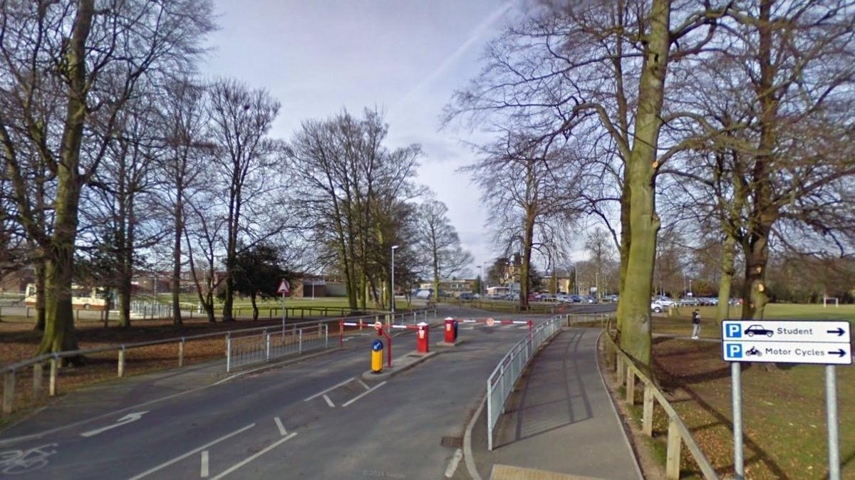 The entrance leading to Cottingham High School, which has security barriers leading to a car park. There are signs pointing to different parking areas. 