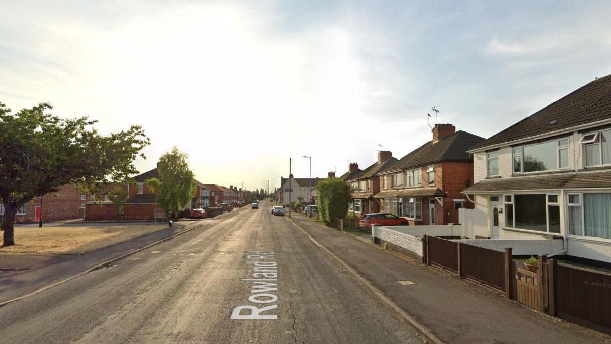 A street with houses on the right. The sky is blue and the sun is shining into the camera. 