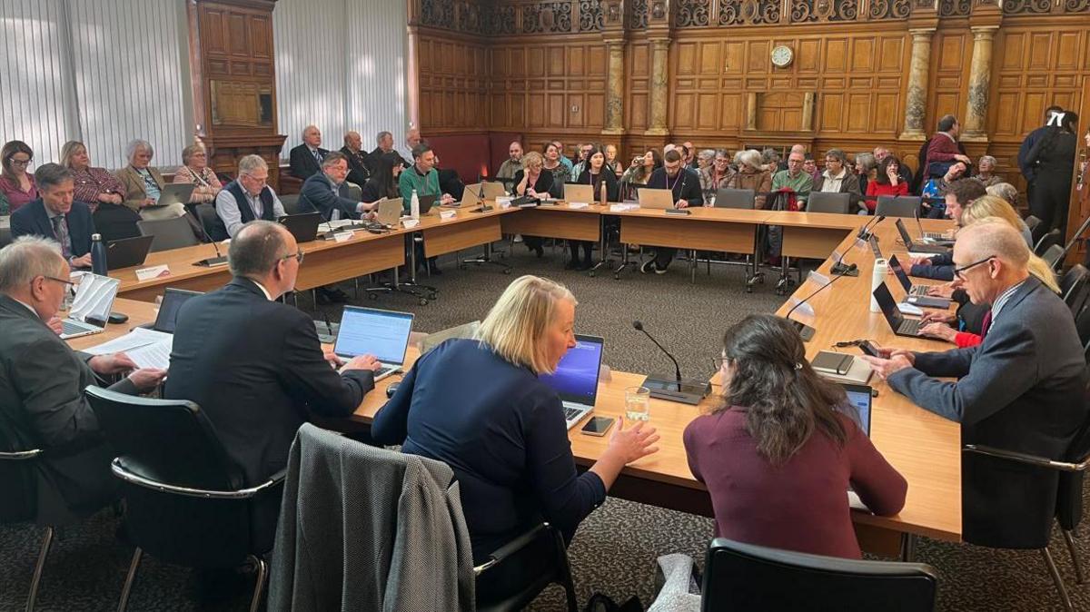 Members of Derbyshire County Council round the cabinet table and members of the public to the end of the packed room.