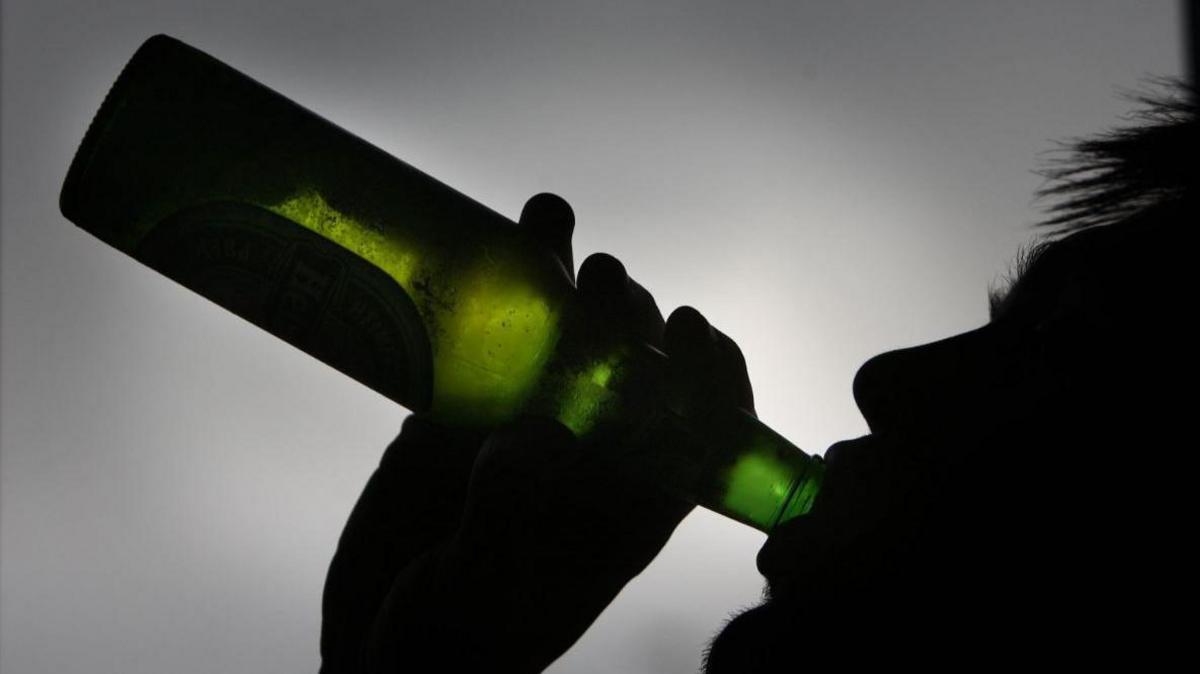 A person drinking from a green glass bottle