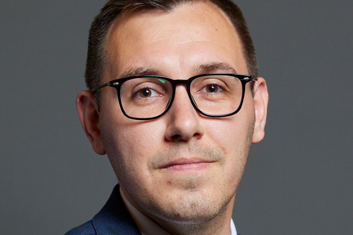 The MP Tom Gordon is pictured in a suit and is wearing glasses. He has short dark hair and a shadow of stubble.