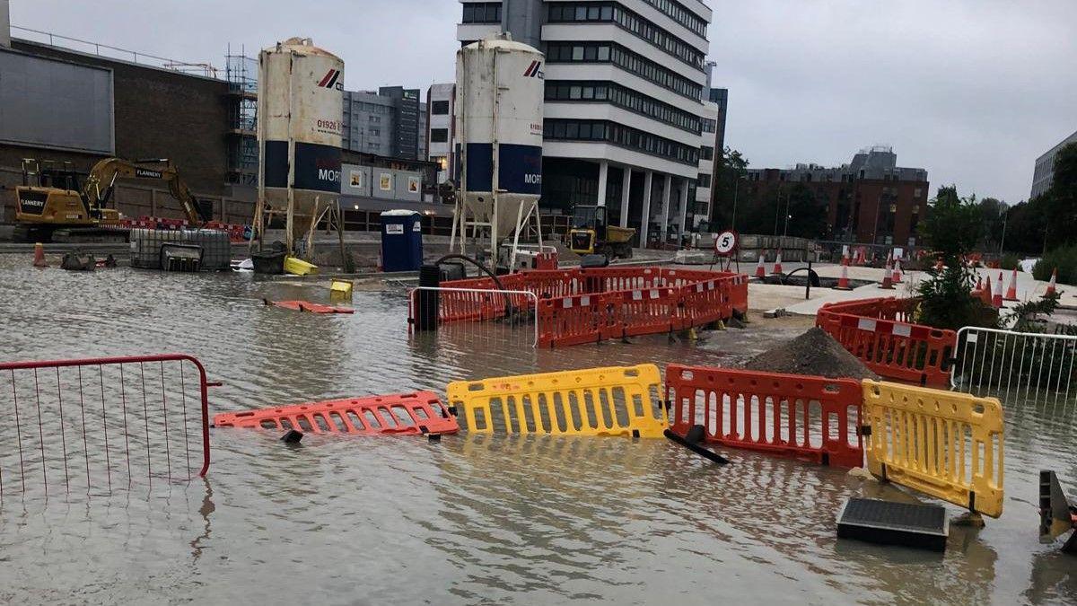 A very large pool of water covering part of Swindon town centre. Temporary barriers can be seen floating in the water