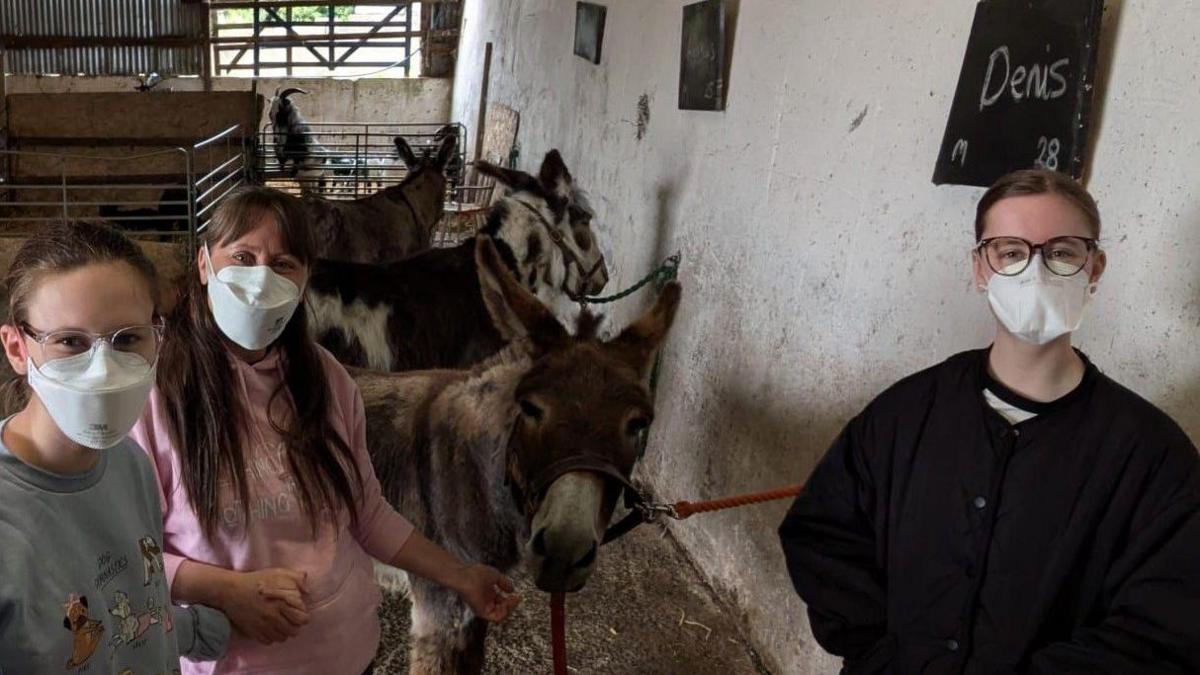 Seren and her mum and sister stand with some donkeys on a day out