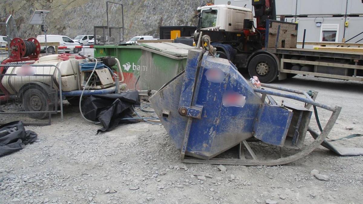 A large blue metal skip is lying on the ground on its side. There are various pieces of industrial equipment around it. A lorry is parked nearby.