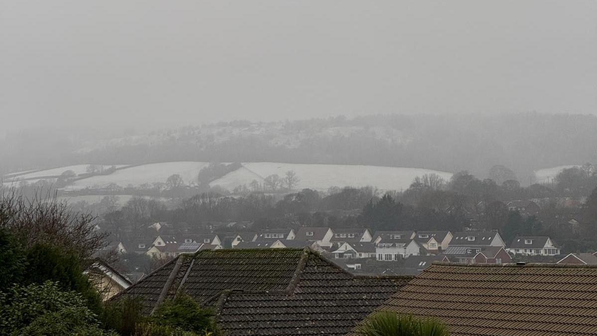 Snow seen in the fields across Sidmouth, there are rooftops which are dry of snow but fields behind it covered