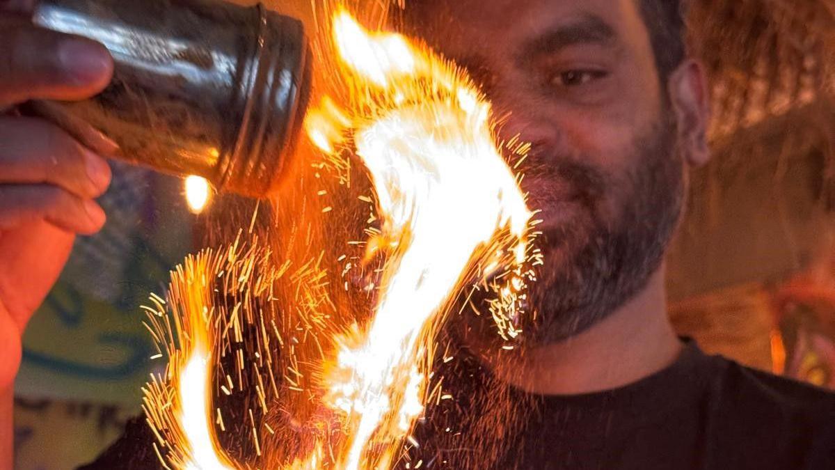 A man stands sprinkling material in a restaurant called the Coconut Tree in Bristol. The thing he is pouring is creating a bright burst of flame