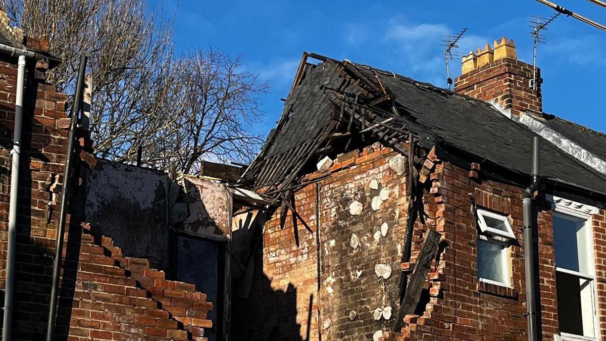 The upper floor of the damaged homes showing a gap where the explosion occurred. The neighbouring house has part of its roof missing. 