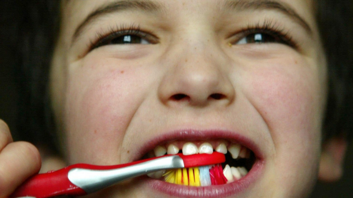 A child brushes their teeth with a colourful toothbrush.