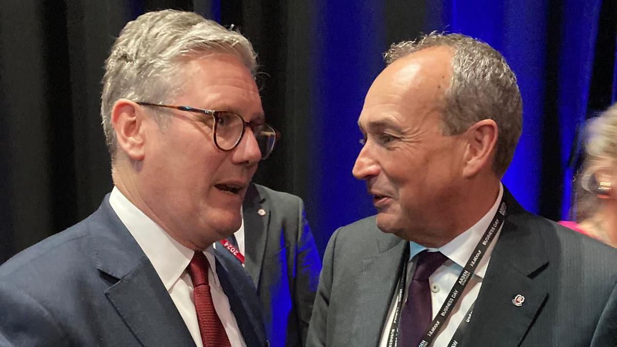 Prime Minister Keir Starmer meeting Jersey Chief Minister Lyndon Farnham - two men with grey hair in suits and white shirt and ties, in close proximity. Man on left is wearing black rimmed glasses and the other is wearing a lanyard around his neck.