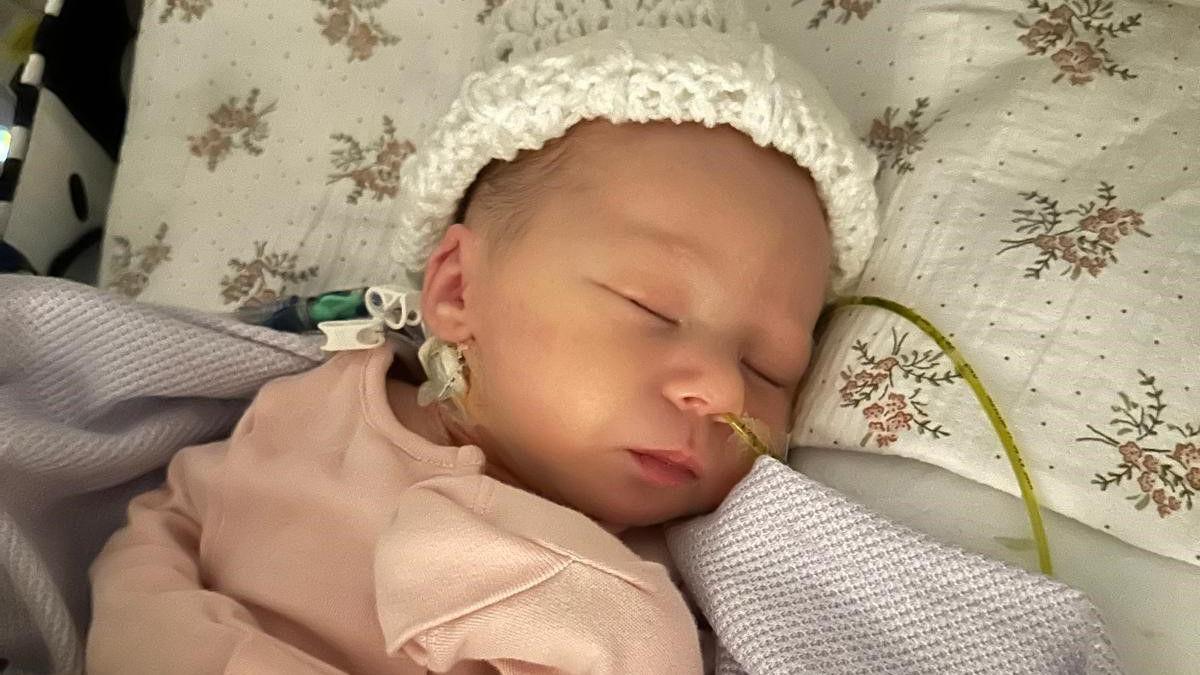 A sleeping baby wearing a white had and pink top.