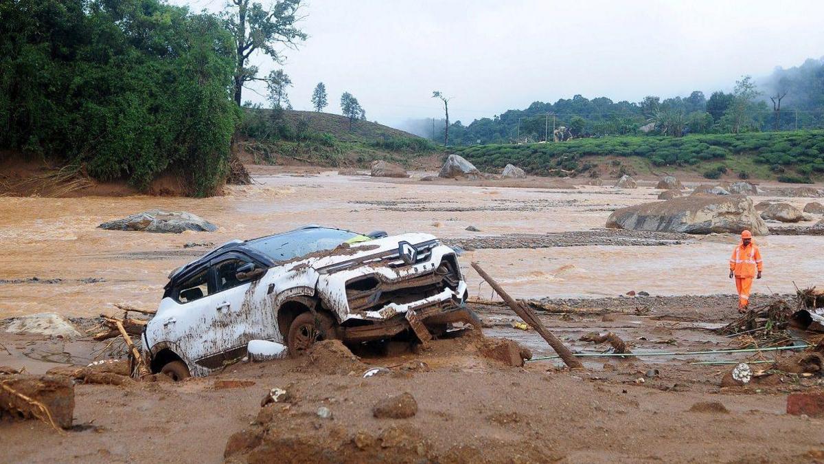 A rescuer walks past a damaged car at a landslide site after multiple landslides in the hills in Wayanad