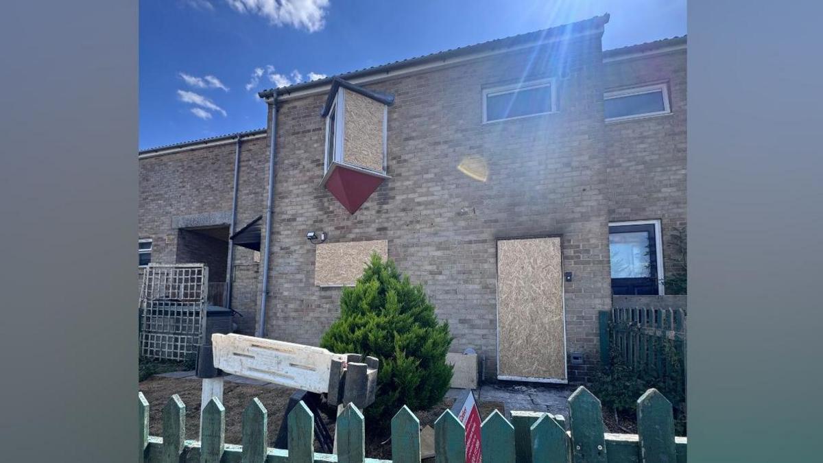 The outside of the house, with the windows and door boarded up.