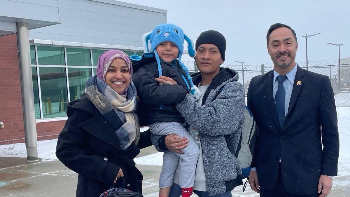 A man holds a five-year-old boy and both are wearing winter hats and smiling, standing outside next to a man and woman who are US congress members