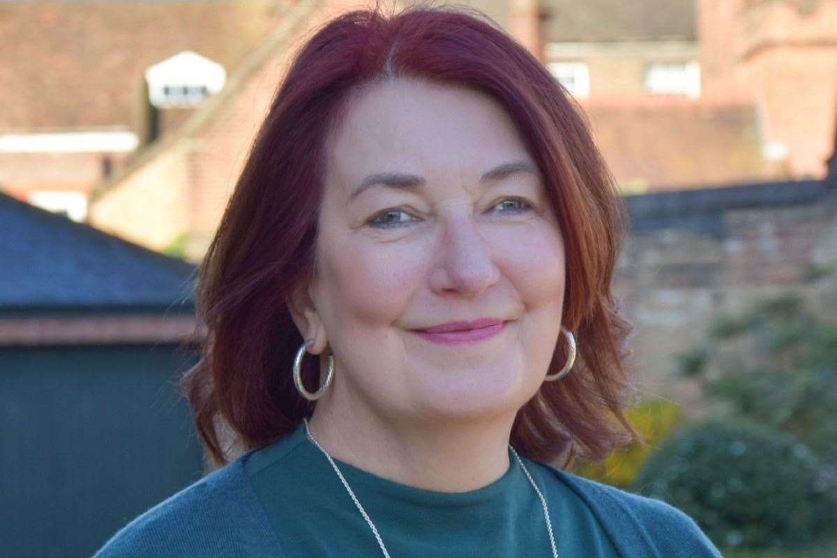 Sue Lintern is wearing a green top. She also had a light necklace and large circular earrings.